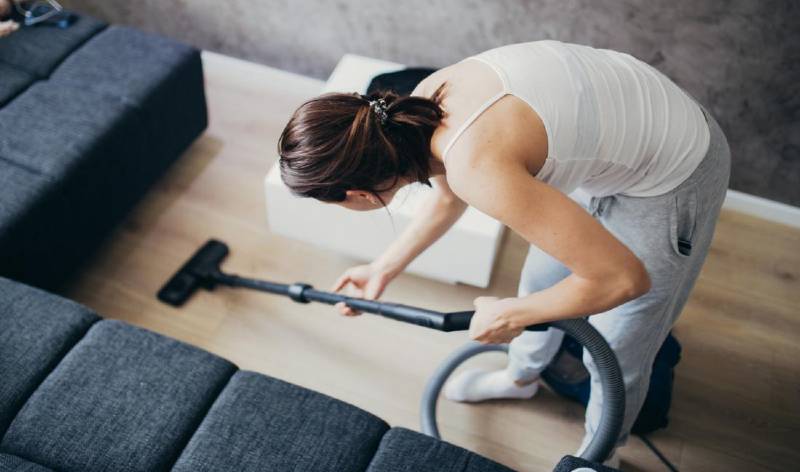 Woman vacuuming with vacuum cleaner inside a room