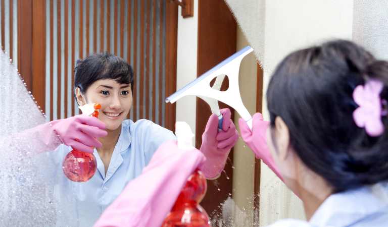 Woman holding a pink bottle in her hand cleaning mirror with brush.