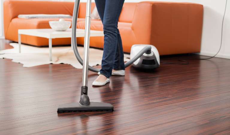 Female is vacuuming floor with vacuum cleaner inside her house.