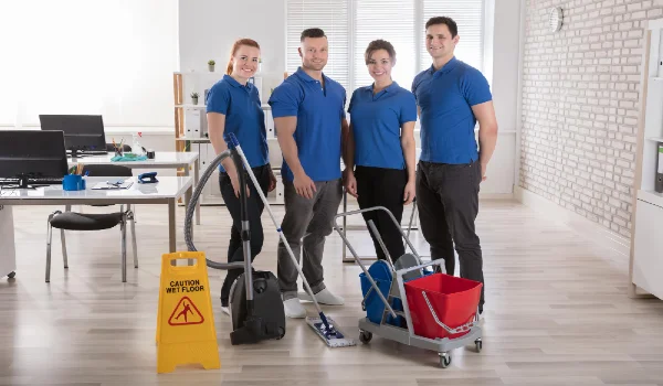 Portrait of smiling janitors with cleaning equipments and caution sign in the office