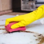 Man cleaning ceramic modern stove or hob with detergent agent hand in yellow gloves clean stove