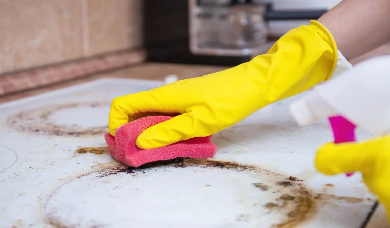 Man cleaning ceramic modern stove or hob with detergent agent hand in yellow gloves clean stove