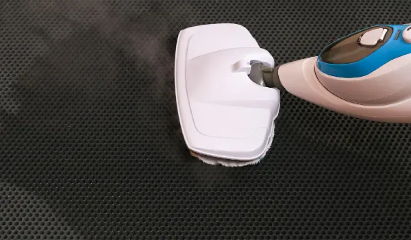 A man washes a black honeycomb door mat with a steam mop killing germs clean floor decontamination
