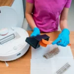 A young woman cleans a robot vacuum cleaner from dirt after cleaning