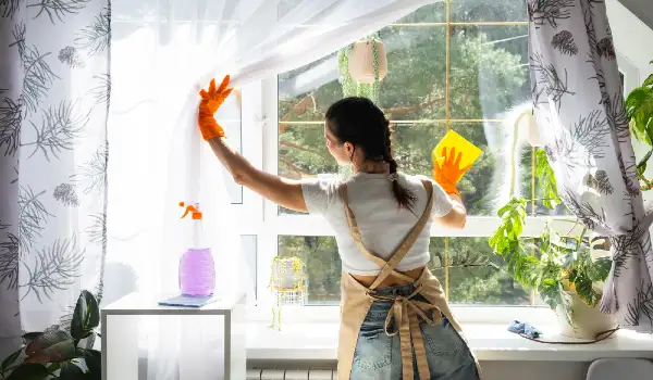 Woman in rubber gloves and apron manually washes window of house with rag cleaner and cleanliness in spring cleaning servise